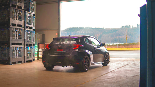 Offside rear view of a lowered black Toyota GR Yaris, in a warehouse looking outside at a rural location, after having the Eibach Pro-Kit fitted