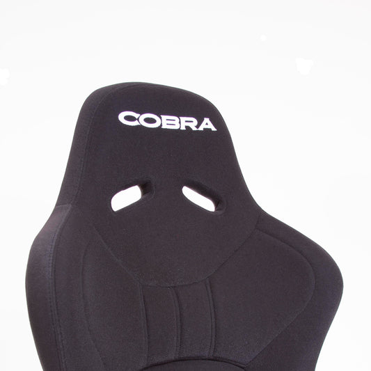 Close up offside front view of a black Cobra Nogaro Club Sports seat with the Cobra name in white, on the headrest