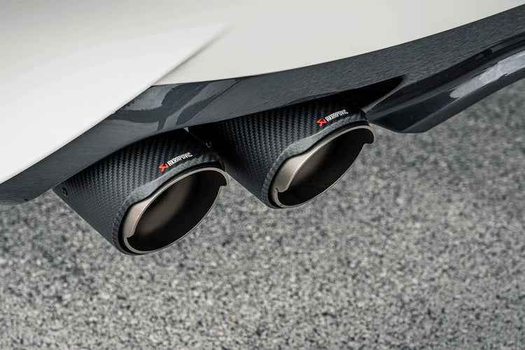 Close up view of a pair of Akrapovič carbon fibre twin pipes & an Akrapovič carbon fibre rear diffuser fitted to a white car