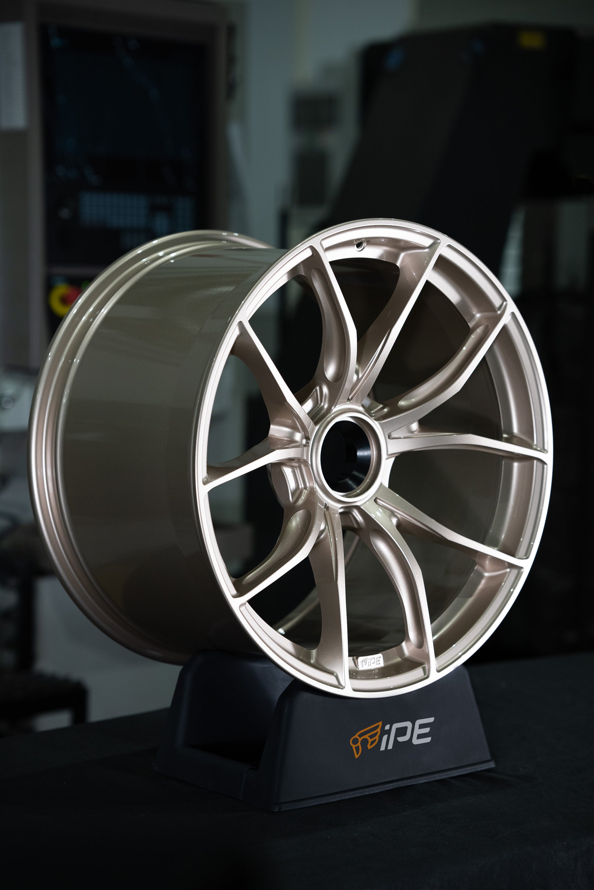 Front side view of an IPE MFR-01 Magnesium wheel in silver with a multi-spoke design sitting on an IPE stand on a worktop with a workshop setting in the background
