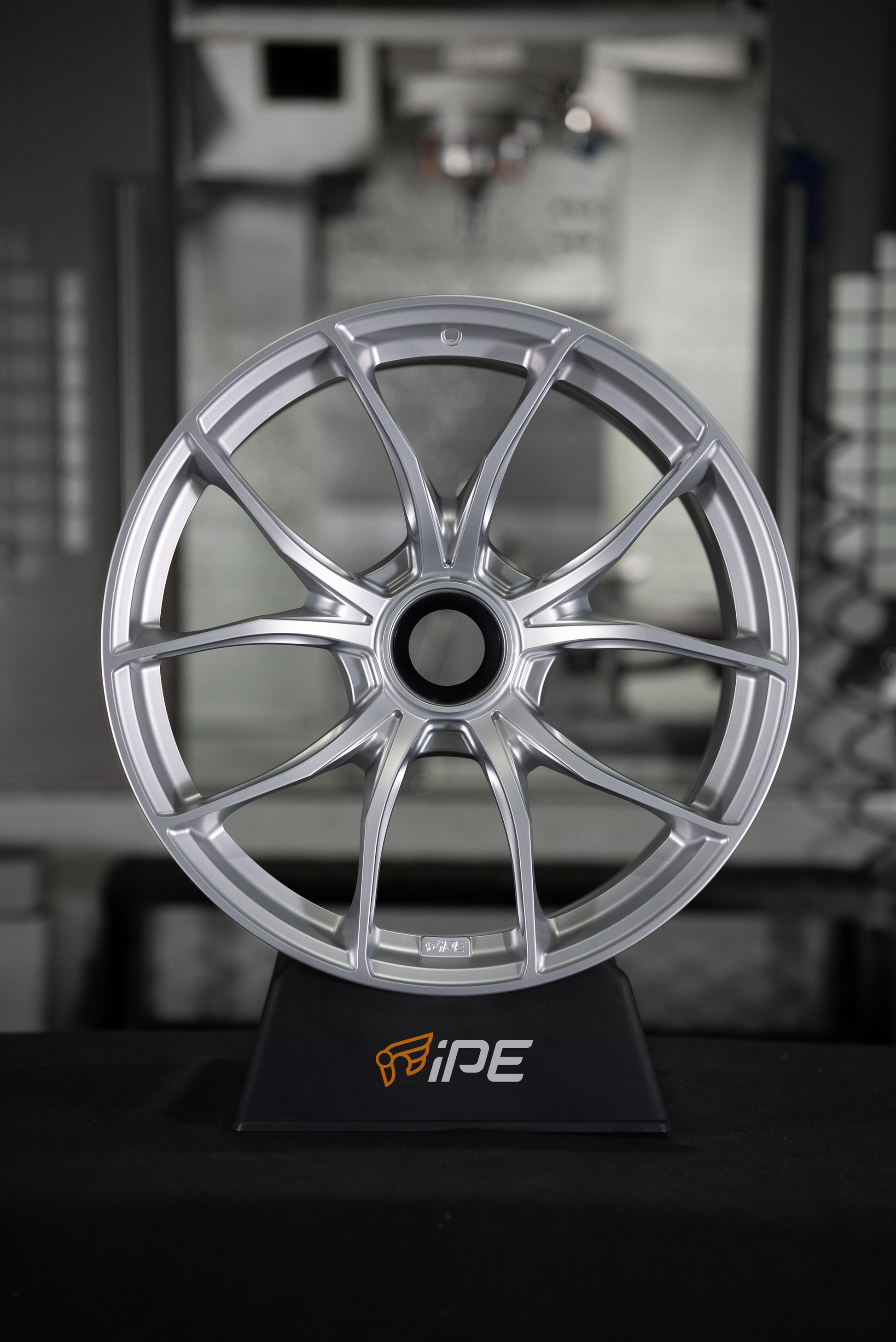 Front view of an IPE MFR-01 Magnesium wheel in silver with a multi-spoke design sitting on an IPE stand with a workshop setting in the background