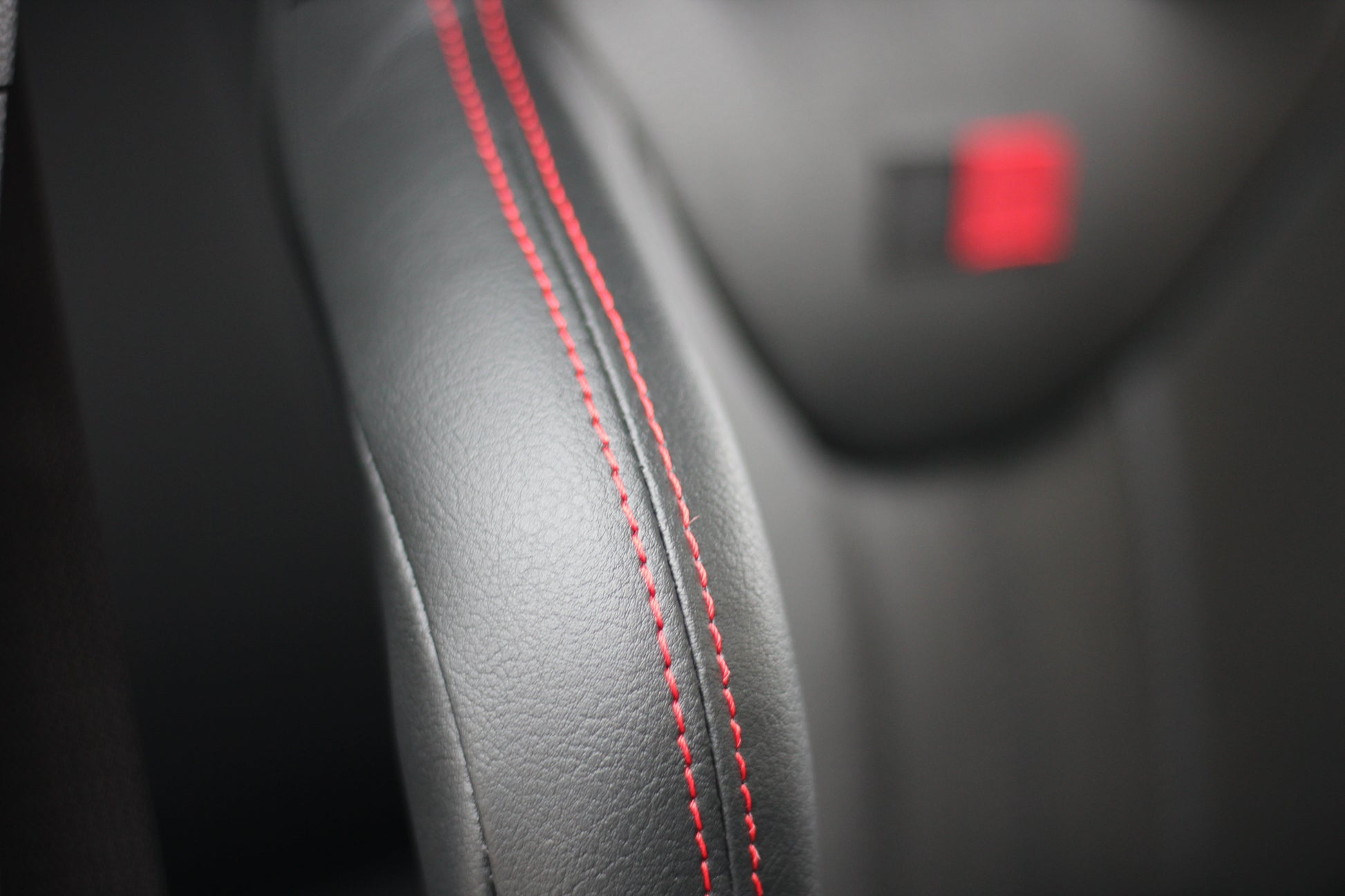 Close of view of the red stitching on a Cobra Nogaro Circuit sports seat & a blurred image of a black & red logo