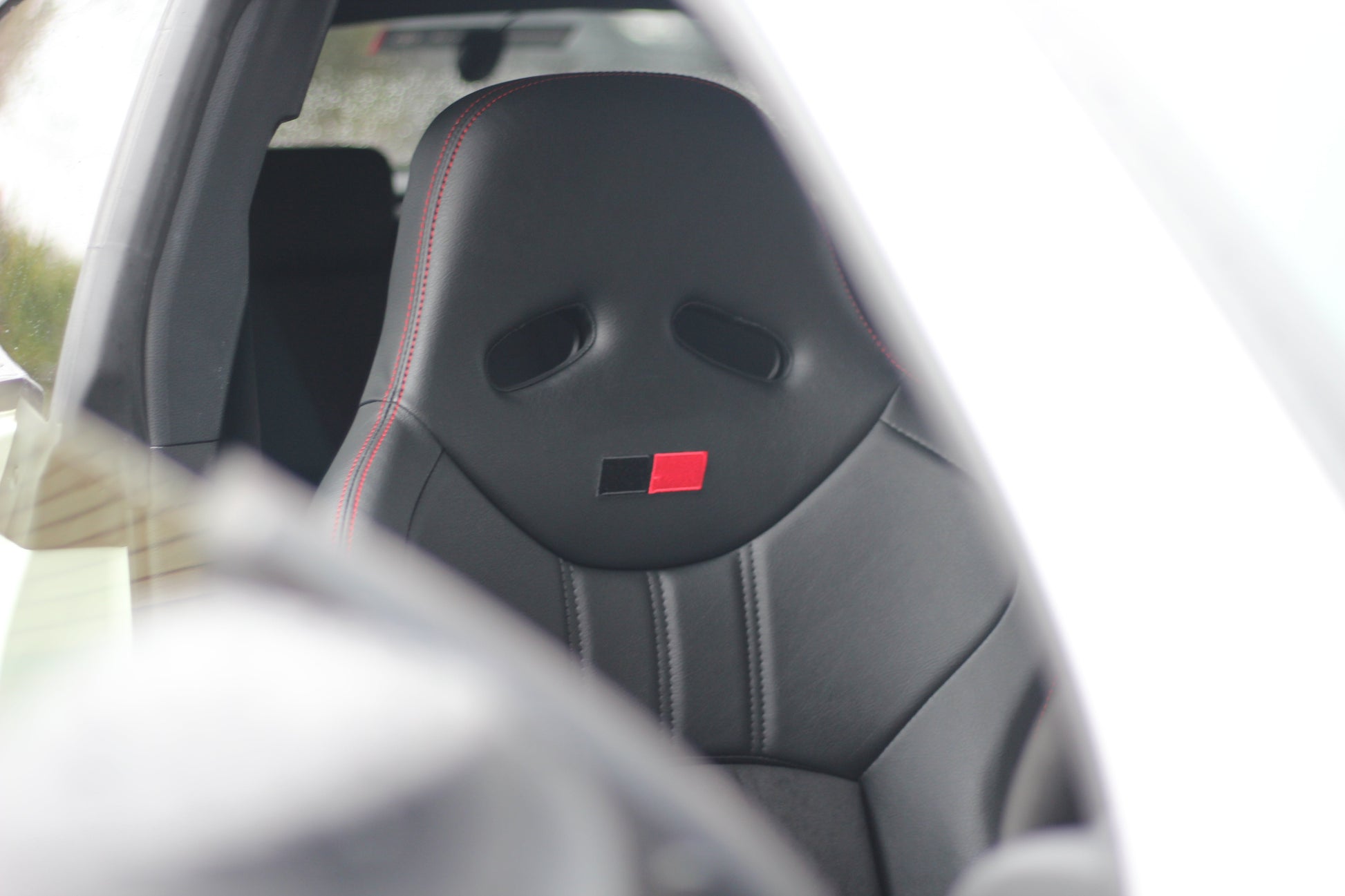 Offside front view of a black Cobra Nogaro Circuit sports seat with red stitching with a red / black emblem on the headrest fitted to a Toyota GR Yaris