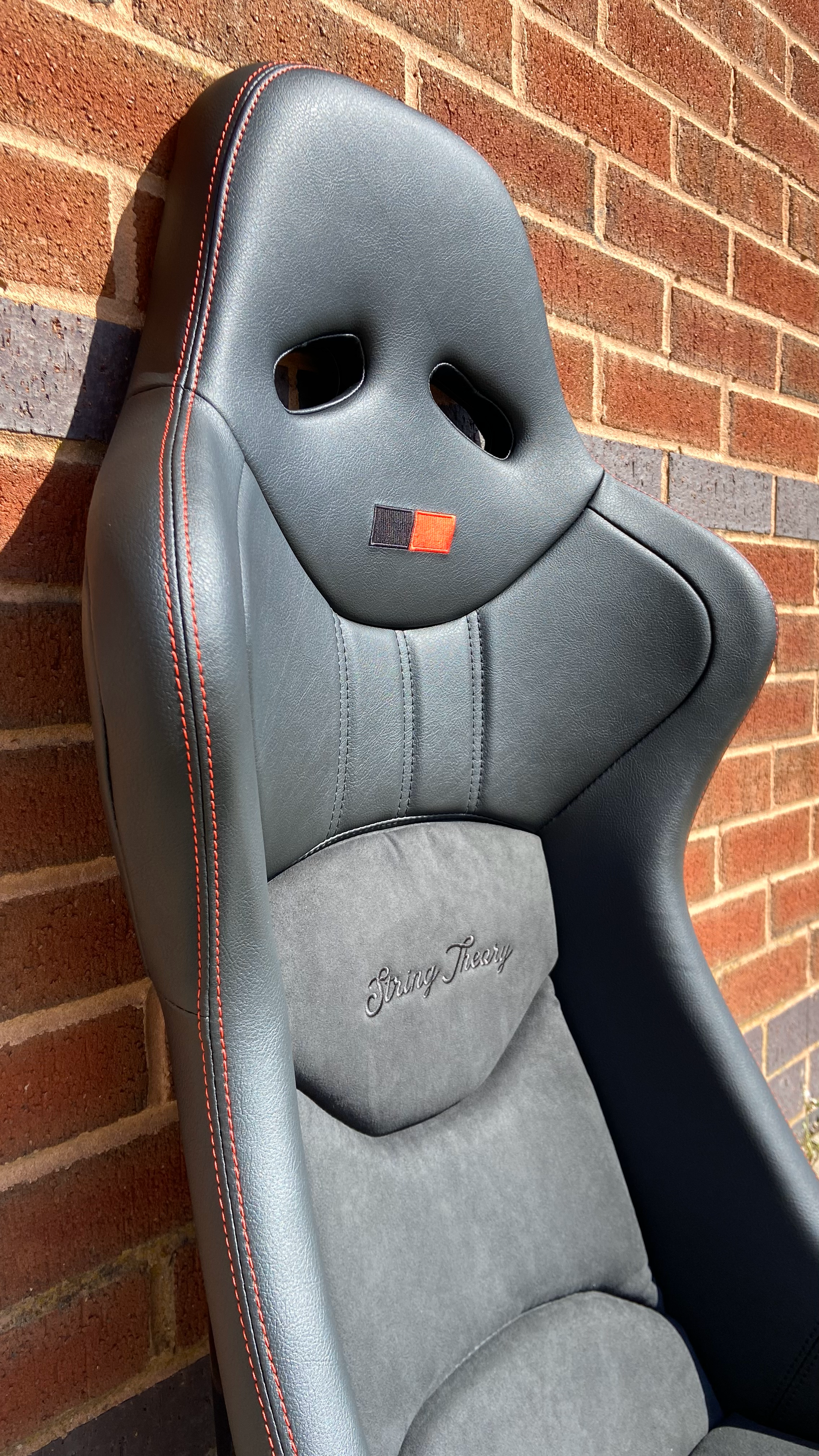 Offside front view of a black Cobra Nogaro Circuit sports seat with red stitching, red / black emblem on the headrest & a String Theory logo sewn into the back rest