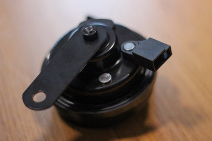 A view of the bottom of a black Hella horn showing the mounting bracket & terminal connector housing