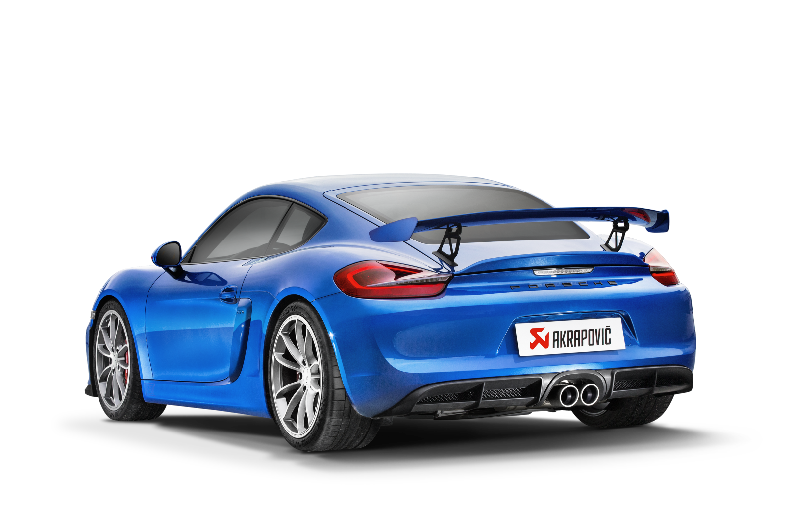 Nearside rear view of a Blue Porsche Cayman 981 GT4 with rear spoiler & an Akrapovič rear exhaust with twin round pipes fitted