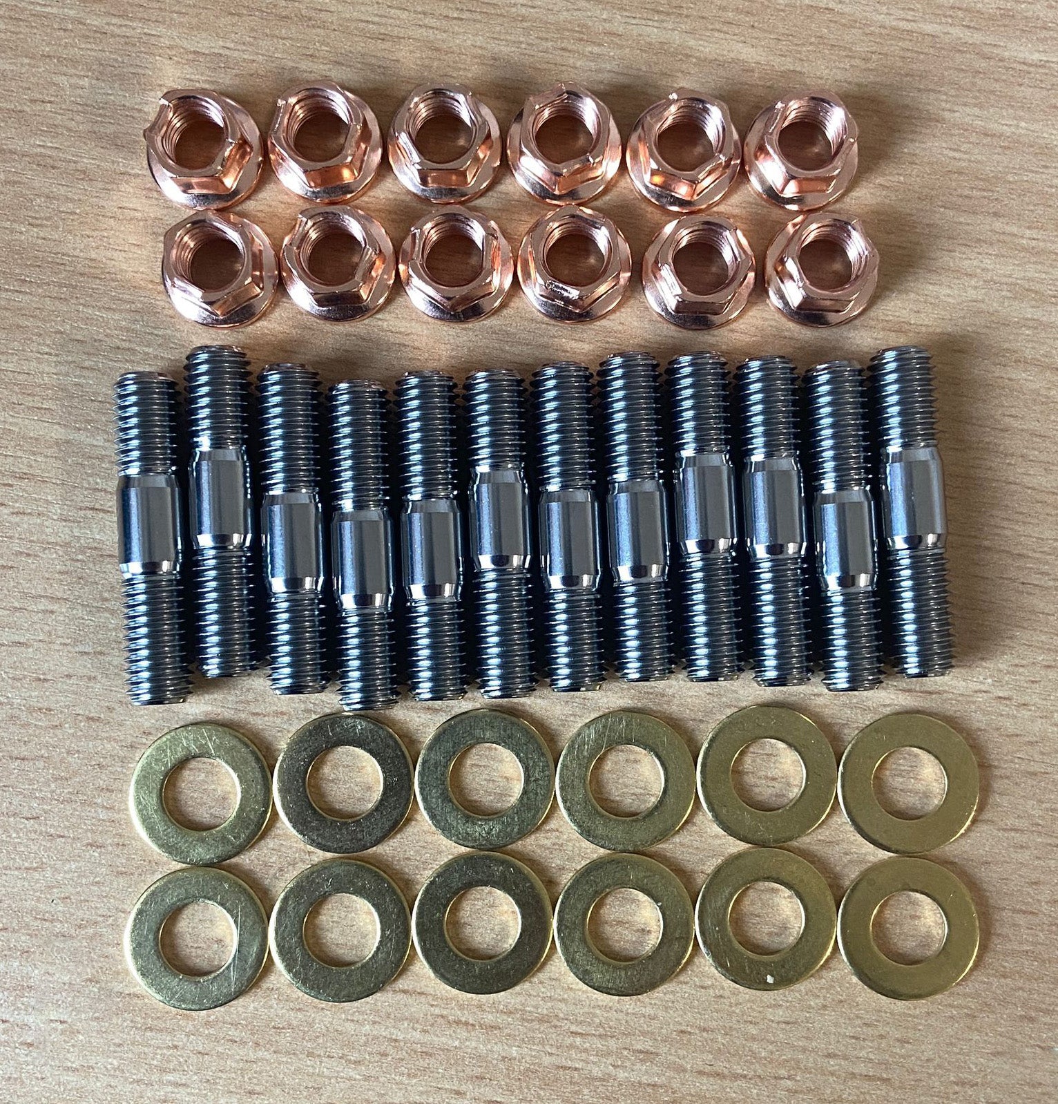 An aerial view of a STG Titanium exhaust manifold stud kit which includes 12 Titanium studs, 12 hex copper K-nuts & 12 brass washers