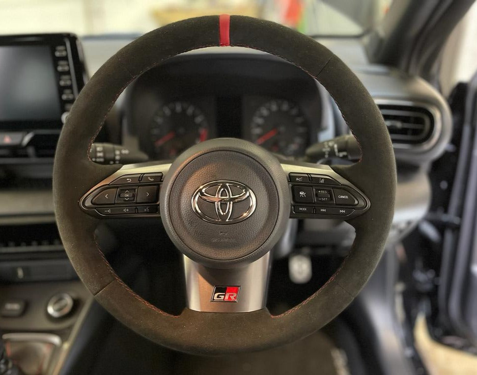 Close up interior view of a Toyota GR Yaris fitted with a black Alcantara steering wheel with Red centre top stripe & stitching