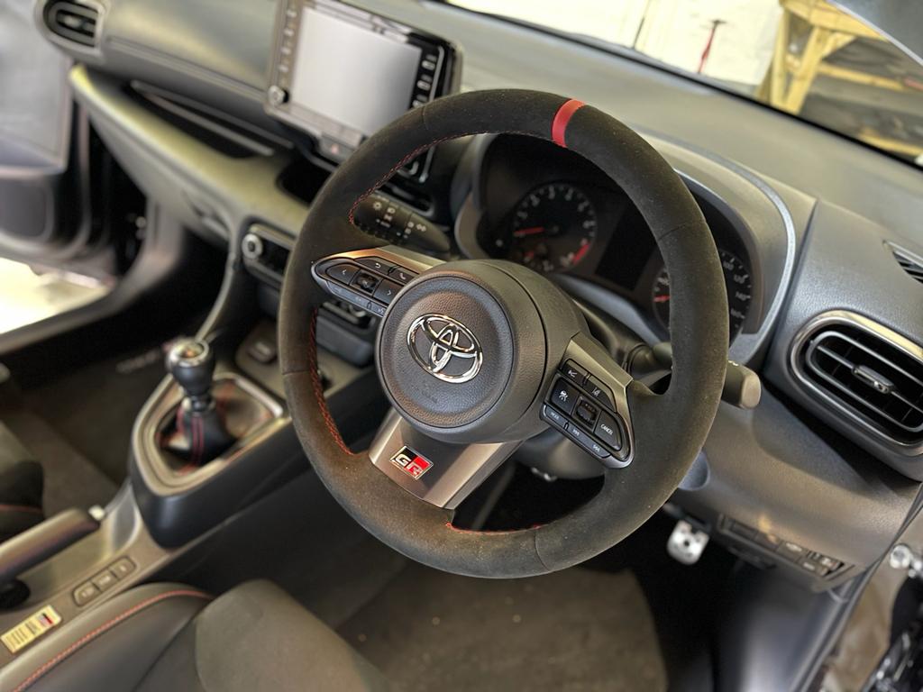Close up interior view of a Toyota GR Yaris fitted with a black Alcantara steering wheel with Red centre top stripe & stitching