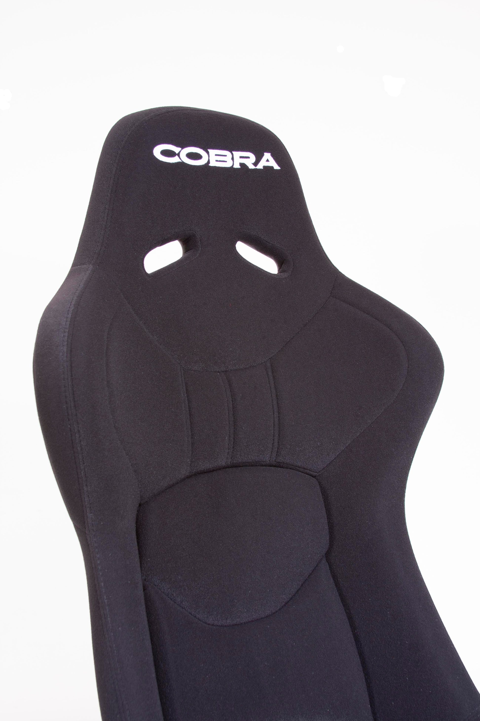 Close up offside front view of a black Cobra Nogaro Club Sports seat with the Cobra name in white, on the headrest